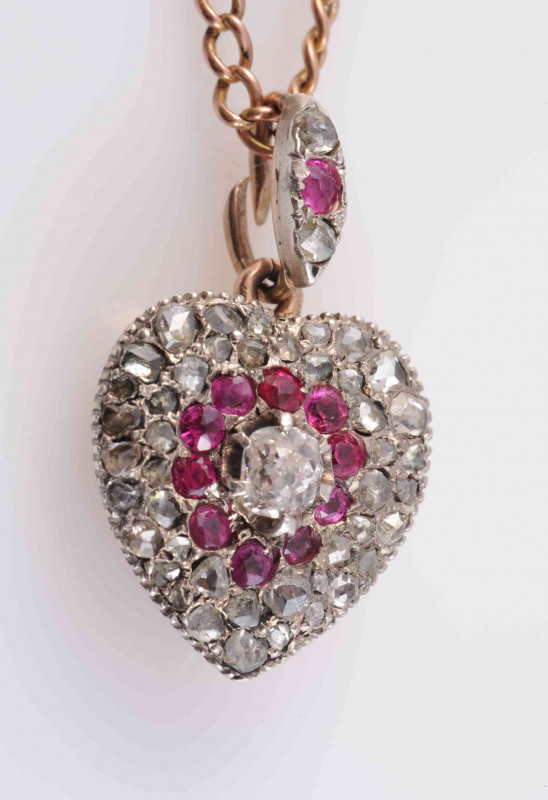 A RUBY AND DIAMOND SET LOCKET PENDANT, circa 1830-1840, the heart shaped pendant set to the centre with a raised claw set old cut diamond highlight, within a surround of ten ruby highlights and graduating old cut diamond highlights, with glass locket to t
