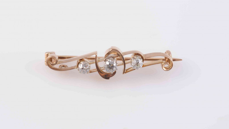 A DIAMOND SET BROOCH, circa 1890-1900, the three graduating old brilliant cut diamonds claw set within an open work mount with coiled metal details, on brooch pin fitting. Weight 4.4gms. Length 4cm.