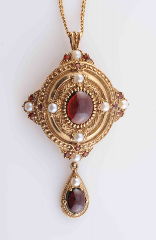 A GARNET AND SEED PEARL BROOCH PENDANT, the domed oval mount set to the centre with an oval cabochon cut garnet within moulded metal work detailing and four evenly spaced seed pearls, in turn within a further surround of moulded scrolling and beaded metal