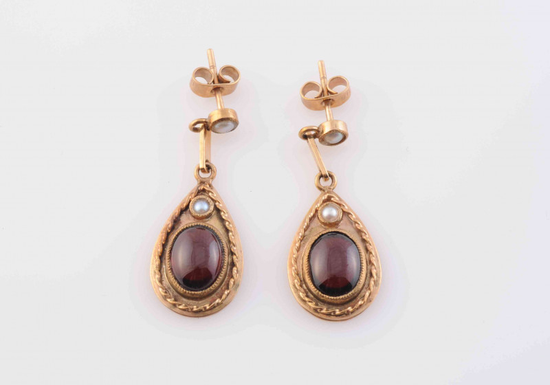 A GARNET AND SEED PEARL BROOCH PENDANT, the domed oval mount set to the centre with an oval cabochon cut garnet within moulded metal work detailing and four evenly spaced seed pearls, in turn within a further surround of moulded scrolling and beaded metal