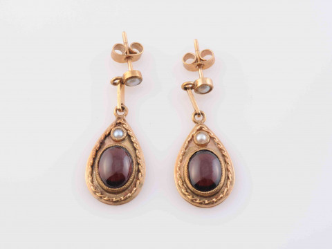 A GARNET AND SEED PEARL BROOCH PENDANT, the domed oval mount set to the centre with an oval cabochon cut garnet within moulded metal work detailing and four evenly spaced seed pearls, in turn within a further surround of moulded scrolling and beaded metal thumbnail