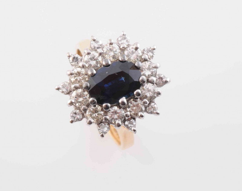 A SAPPHIRE AND DIAMOND RING, the oval cut sapphire claw set within a surround of ten brilliant cut claw set diamonds, in turn within an outer surround of ten evenly spaced brilliant cut diamond highlights, all set raised in an open work mount between open