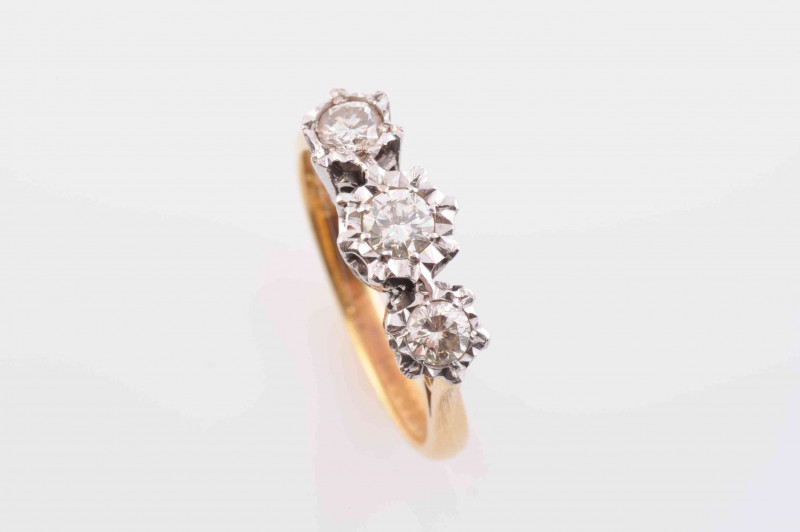 A DIAMOND RING, the three graduating brilliant cut diamonds each set in heavy claw settings with pierced detail mounts, between similarly pierced tapering shoulders on a plain band. Stamped 18. Makers mark H.S. Ring size M. Weight 3.9 grams.