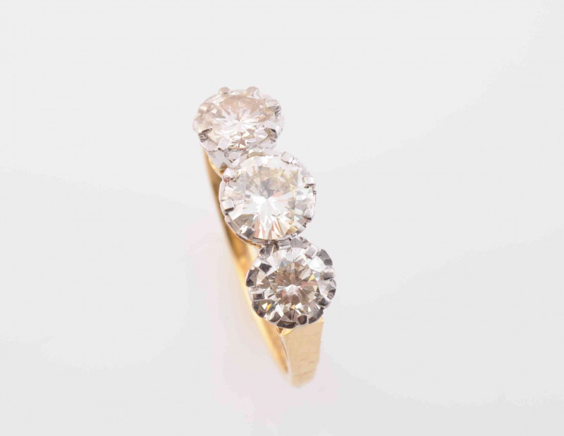 A DIAMOND RING, the three slightly graduating brilliant cut diamonds each claw set in pierced detail mounts between similarly pierced tapering shoulders on a plain band. Stamped 750. Makers marks H&M. Ring size M. Weight 3.5 grams.