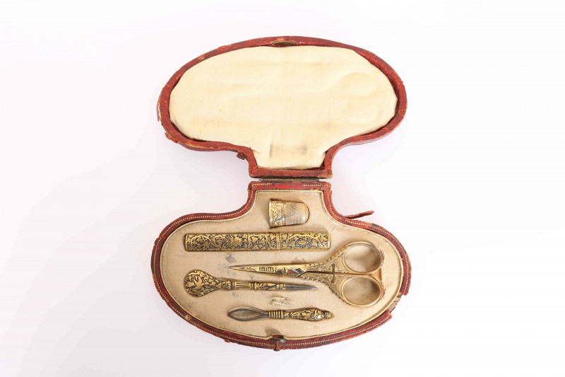 A 19TH CENTURY ETUI, comprising gold damascened needle case, leather point, loop threader, each test as 22 carat gold decorated; a cast yellow metal thimble, tests as 14ct gold; a pair of gilt metal handled scissors, all in a shaped gilt-tooled leather ca