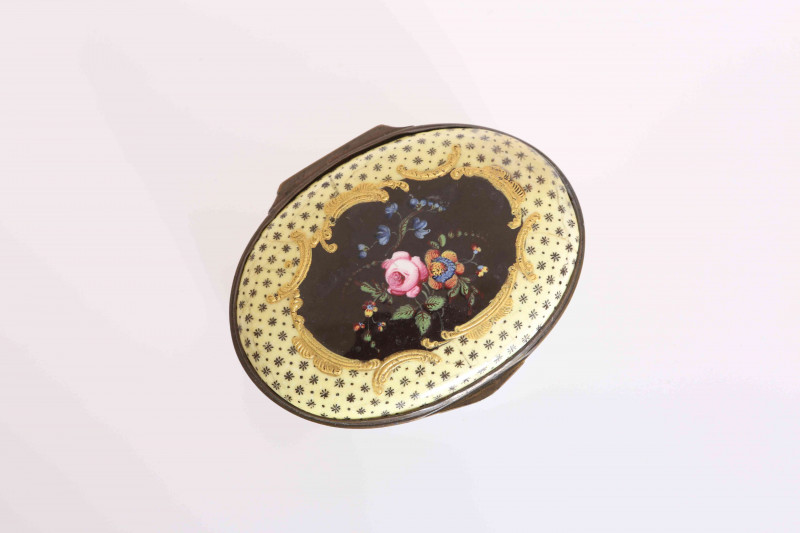 A SOUTH STAFFORDSHIRE ENAMEL SNUFF BOX, CIRCA 1775, oval, the hinged cover centred by a floral spray in polychrome enamels within a frame of tooled gilt C-scrolls, the yellow ground with floral bosses, the sides similarly decorated. 7.5cm by 6cm