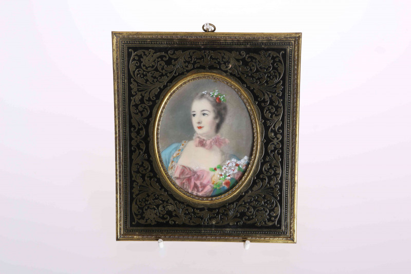 A PORTRAIT MINIATURE IN A BRASS FRAME, depicting a lady with flowers in her hair, the frame decorated with scrolling foliage. Overall 14cm by 12.5cm