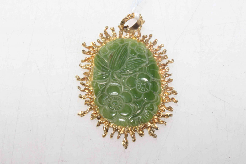 A Chinese carved jade pendant, the oval jade plaque carved with flowerheads and leaves, the mount with irregular edge, the bale stamped 750, 5.5cm by 4cm.